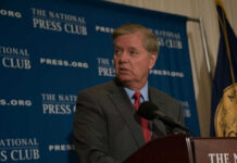 Bridge-Builder Gone—Who Steps In? Man in suit speaking at a podium with a microphone