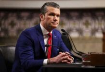 Hegseth Pulls Plug—Why Now? Man in blue suit speaking at a microphone