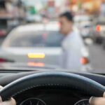 Shelters Overrun — Car Camp Survival Begins Driver’s hands on steering wheel as a pedestrian crosses in front of a car in traffic