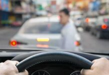 Shelters Overrun — Car Camp Survival Begins Driver’s hands on steering wheel as a pedestrian crosses in front of a car in traffic
