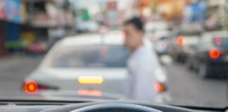 Driver’s hands on steering wheel as a pedestrian crosses in front of a car in traffic