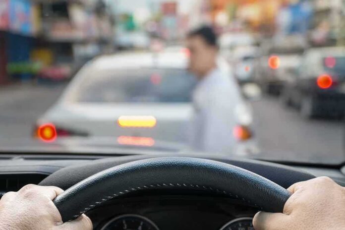 shutterstock_1056108380 Driver’s hands on steering wheel as a pedestrian crosses in front of a car in traffic