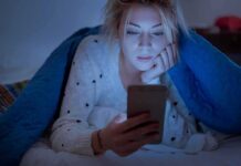 Gen Z Interview Habits Spark Employer Fury Woman under a blanket looking at a smartphone in bed