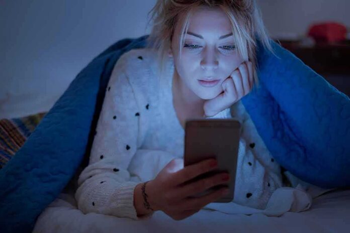 shutterstock_1129353881 Woman under a blanket looking at a smartphone in bed