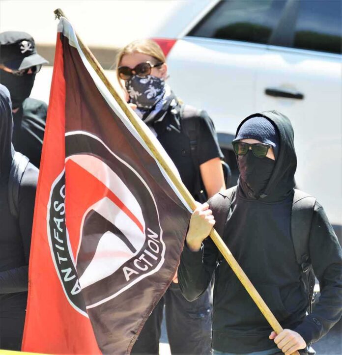 shutterstock_1472772446 Masked protesters holding a black and red flag