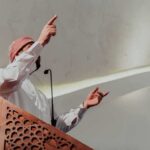 Shock Move: Archbishop Endorses Mosque Plan Speaker in traditional attire gesturing from a carved wooden podium