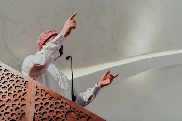 shutterstock_2243335319 Speaker in traditional attire gesturing from a carved wooden podium
