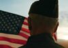 Coalition Targets The Suicide Risk VA Overlooks A veteran in uniform standing in front of an American flag at sunset