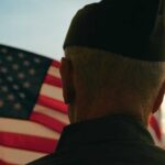 Coalition Targets The Suicide Risk VA Overlooks A veteran in uniform standing in front of an American flag at sunset