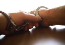 Crowded Con Turns Predators’ Playground Close-up of a handcuff being secured on a wrist