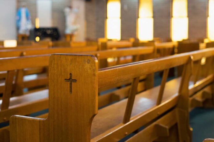 Wooden,Church,Pews,With,A,Carved,Cross,In,A,Softly Wooden church pew with carved cross in a sunlit sanctuary