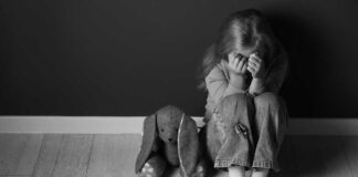 Child sitting on floor with face in hands beside stuffed bunny