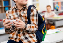 Beijing’s Quiet Invasion Hits Classrooms Child with smartphone and backpack sitting in classroom