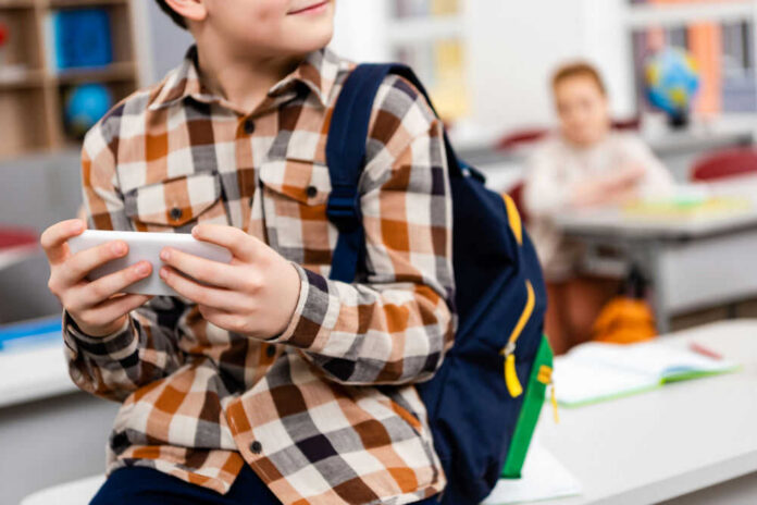 smartphone-at-school252410888jpg Child with smartphone and backpack sitting in classroom