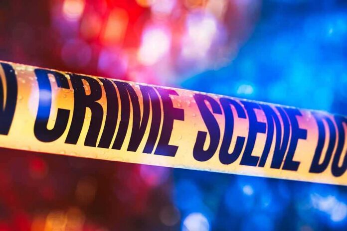 shutterstock_1019899543 Crime scene tape with blurred emergency lights in background