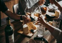 Hands toasting wine glasses over a cheese board