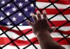 Hand reaching through fence toward American flag