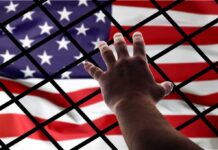 Hand reaching through fence toward American flag