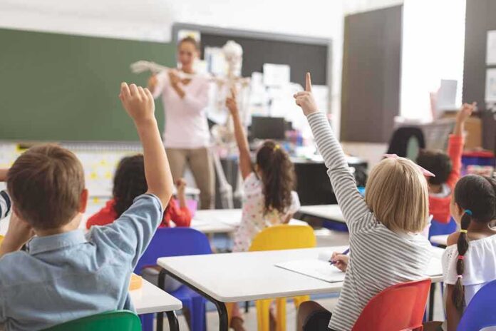 Elementary students raise hands in a classroom