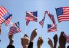 Hands waving American flags against a blue sky