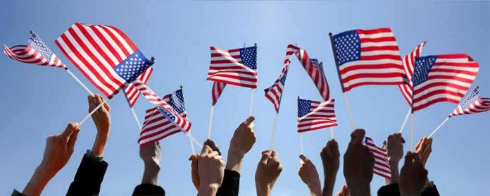 Hands waving American flags against a blue sky