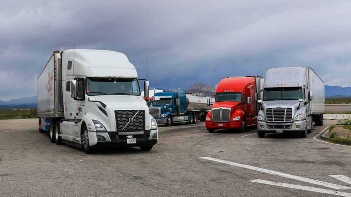 shutterstock_1409829773 Semi trucks parked at a rest area under cloudy sky