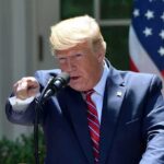 Trump Threat: Help Iran, Lose Everything speaker at podium pointing during outdoor press event