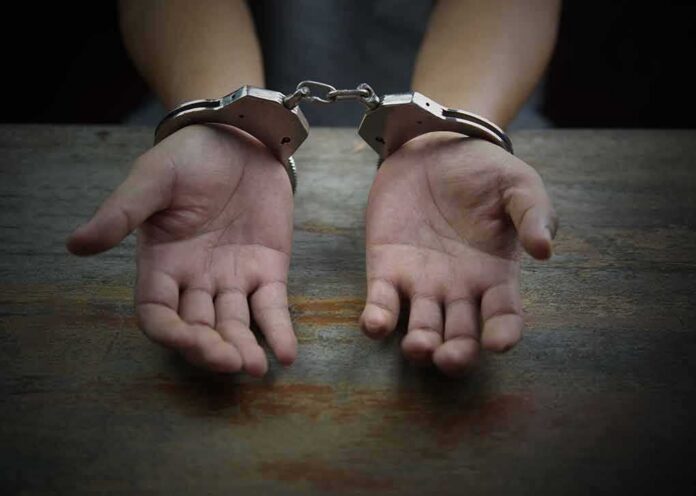 Hands in handcuffs on a wooden table