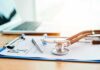 Stethoscope on a prescription form beside a pen and laptop