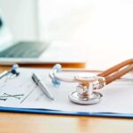 Stethoscope on a prescription form beside a pen and laptop