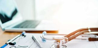 Stethoscope on a prescription form beside a pen and laptop