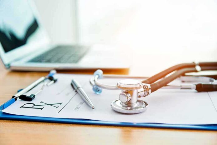 Stethoscope on a prescription form beside a pen and laptop