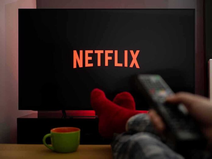 shutterstock_1680823216 TV screen with Netflix logo and person holding remote