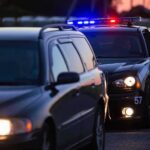 Police car with flashing lights behind a stopped vehicle at dusk