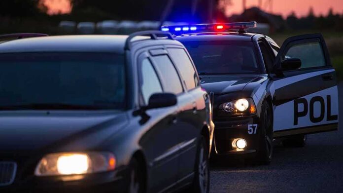 Police car with flashing lights behind a stopped vehicle at dusk