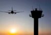 Airplane approaching runway near airport control tower at sunset