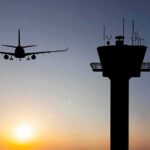 Airplane approaching runway near airport control tower at sunset