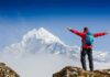 Bible Fight Erupts Over Everest Fossils Hiker with arms raised facing snowy mountain peak