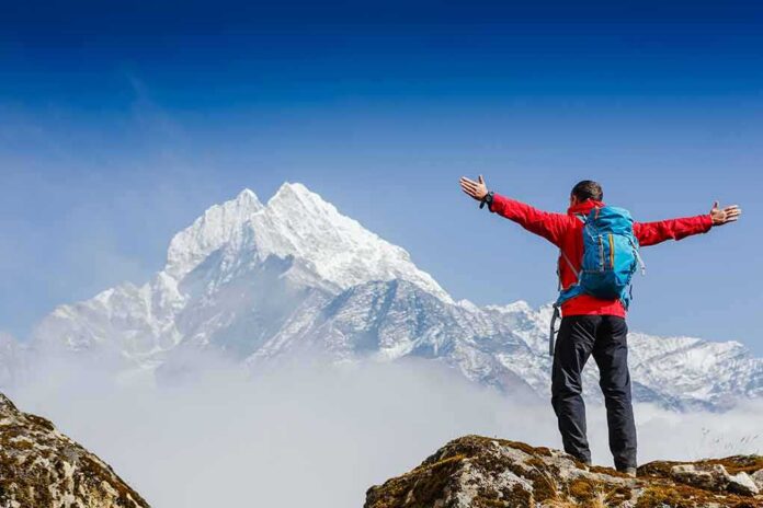 shutterstock_360405170 Hiker with arms raised facing snowy mountain peak