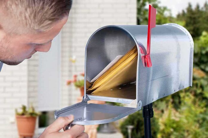 shutterstock_725071210-2 man checking mail in an open curbside mailbox