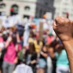 Champagne Socialism Meets Picket Line Raised fist in foreground at a crowded street protest