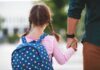 Girl with backpack holding an adult's hand