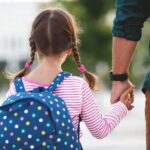 Girl with backpack holding an adult's hand