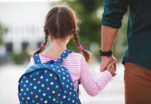 Girl with backpack holding an adult's hand