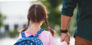 Girl with backpack holding an adult's hand