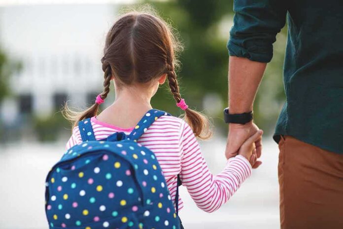 shutterstock_1151079065-1 Girl with backpack holding an adult's hand