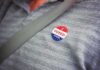 Election Crackdown – DOJ Blitz Targets Noncitizen Ballots I voted sticker on a gray shirt under a seat belt