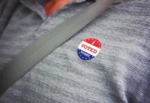 Election Crackdown – DOJ Blitz Targets Noncitizen Ballots I voted sticker on a gray shirt under a seat belt