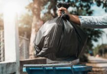 Hand dropping a black garbage bag into a blue bin