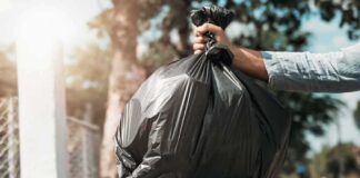 Hand dropping a black garbage bag into a blue bin